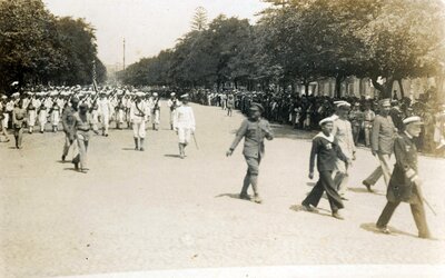 U.S. naval men marching with a flag on a tree-lined boulevard with crowds looking on